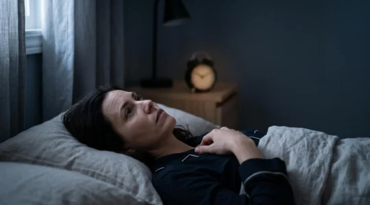 Personne allongée dans un lit dans la pénombre, les yeux ouverts, dans une chambre calme et minimaliste au milieu de la nuit